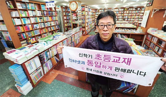 ▲ 문인홍 인천시 서점조합장이 자신이 운영하고 있는 연수구 대일문고 매장에서 새학기 교재를 인터넷과 동일하게 판매한다는 플래카드를 펼치고 있다