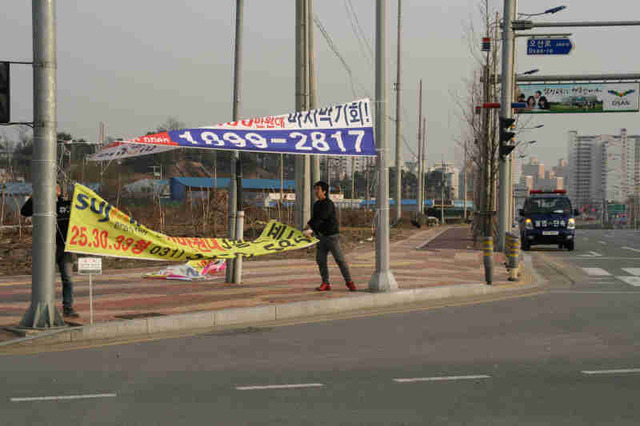 ▲ 오산시내 주요 교차로에 아파트 분양을 광고하는 불법 현수막이 무분별하게 내걸려 시 공무원과 용역업체, 공공근로자 등이 현수막을 단속수거하고 있다.