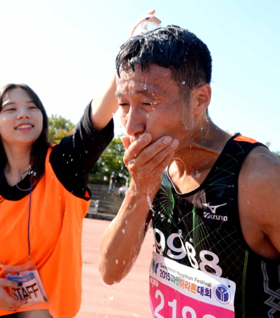 13일 과천 관문체육공원 운동장에서 열린 ‘2015 과천 마라톤 대회’에서 더위에 지친 참가자 머리에  시원한 물을 뿌려주고 있다.전형민기자
