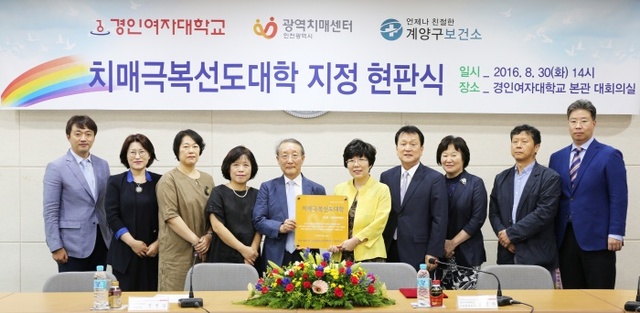 ▲ 경인여대가 최근 치매극복선도대학으로 지정, 관계자들이 현판식을 갖고 기념촬영을 하고 있다