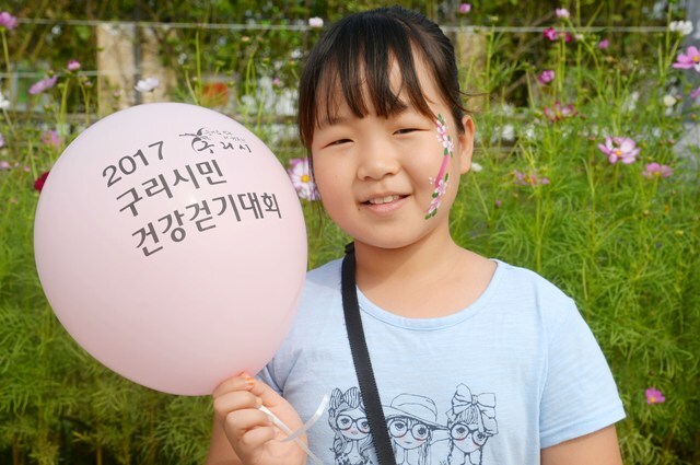 ▲ 코스모스가 만개한 청명한 가을날 가족, 연인과 함께 아름다운 추억을 만들 수 있는 ‘2017 구리시민 건강 걷기대회’가 24일 구리한강시민공원에서 성황리에 개최되었다. 얼굴에 페이스페인팅을 한 어린이가 풍선을 들고 환하게 웃고 있다. 이번 행사는 구리시 주최, 경기일보·구리시체육회가 주관했다. 조태형기자