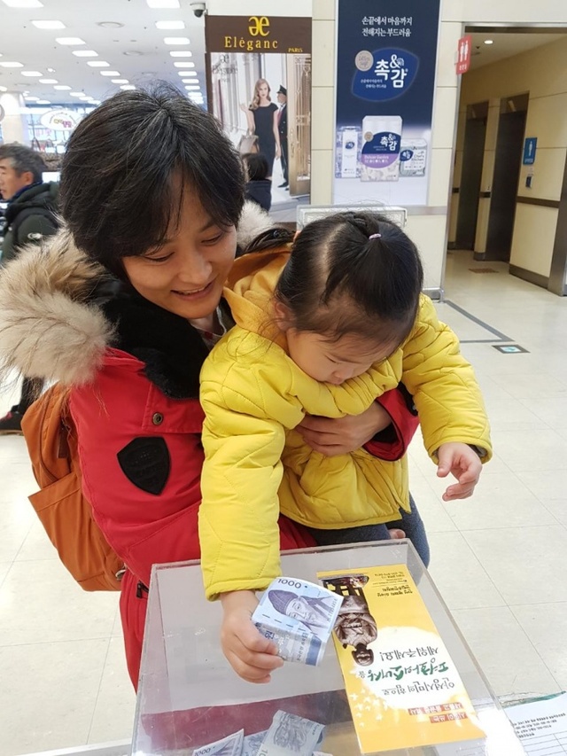 ▲ 소녀상 건립을 위한 거리모금에서 한 시민이 자녀를 안고 모금에 동참하고 있다. 평화의 소녀상 건립 추진위 제공
