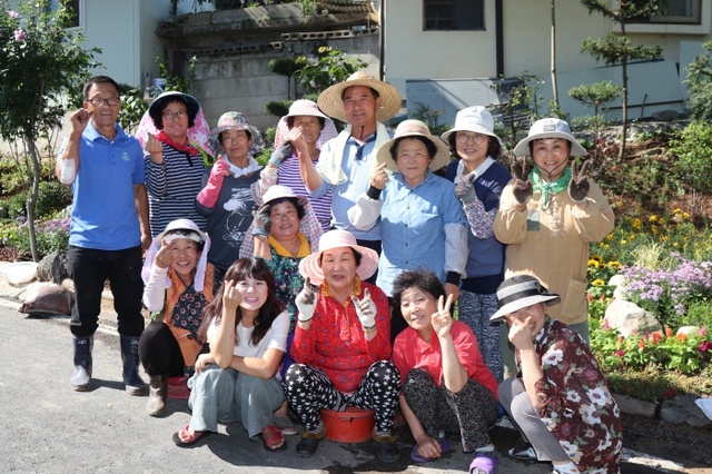 ▲ 마을 안길 도로변 꽃밭을 가꾸던 송현1리 주민들과 정성훈 이장(가운데 밀집 모자 쓴 이)이 잠시 짬을 내어 카메라 앞에 모였다.