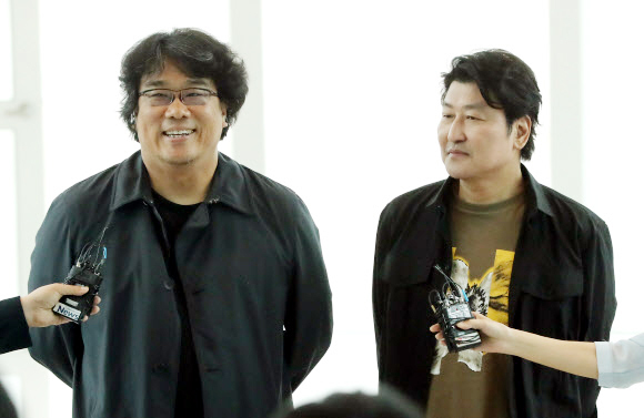 영화 기생충으로 칸 영화제에서 황금종려상을 받은 봉준호 감독이 27일 인천국제공항으로 입국, 취재진의 질문에 답변하고 있다. 오른쪽 배우 송강호. 연합뉴스