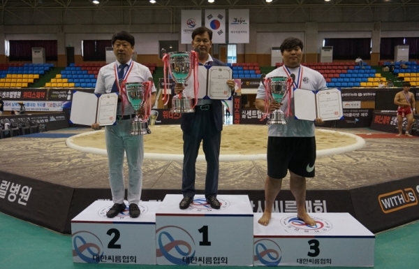 제주특별자치도 성산국민체육센터에서 열린 제33회 전국시도대항장사씨름대회에서 2년 만에 종합우승을 차지한 경기도씨름협회의 김준태 전무이사(가운데)가 우승트로피를 들고 시상대 가장 높은 곳에 올라있다.대한씨름협회 제공-copy(o)1