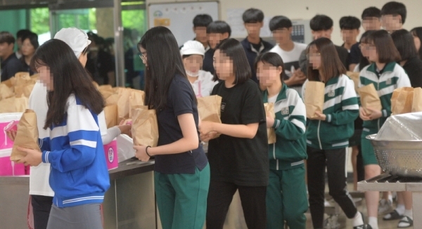 학교비정규직 노동자들의 총파업이 시작된 3일 오후 인천 서구 한 고등학교 급식실에서 학생들이 대체급식으로 제공된 빵과 음료 등이 든 봉투를 받고 있다.조주현기자