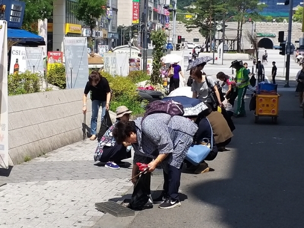 지난 8일 수원영통중심상가의 한 도로에서 환경관리원 및 자원봉사자들이 각종 쓰레기로 막혀있는 빗물받이를 청소하고 있다. 이연우기자