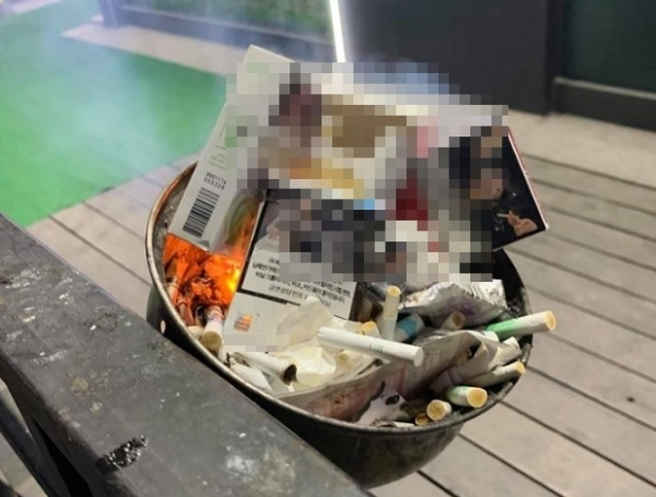 길거리에 설치된 재떨이에서 담배꽁초로 인해 쓰레기에 불이 붙어 연기를 내뿜고 있다. 온라인 커뮤니티