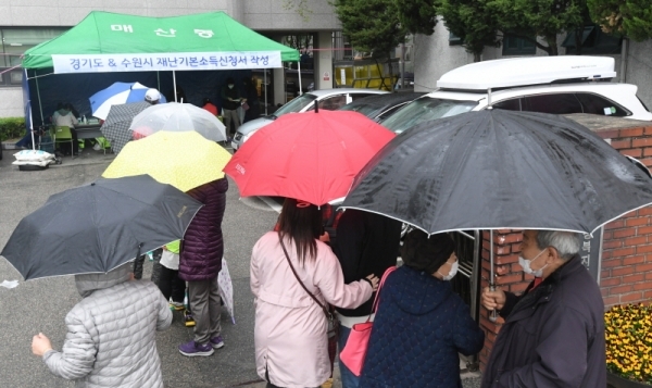 경기도재난기본소득 현장신청이 시작된 20일 오후 매산동행정복지센터에서 궂은 날씨에도 현장을 찾은 시민이 우산을 쓰고 늘어서 있다.조주현기자