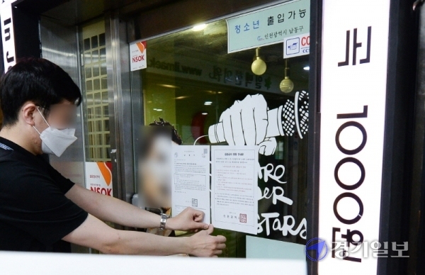 코로나19 확진 판정을 받은 인천 학원강사를 고리로 지역 감염이 확산하자, 인천시가 관내 코인노래방에 2주간 집합금지 명령을 내린 21일 남동구청 관계자가 구월동 로데오거리의 한 코인 노래방 출입문에 집합금지 명령 안내문을 붙이고 있다. 장용준기자