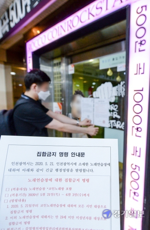 코로나19 확진 판정을 받은 인천 학원강사를 고리로 지역 감염이 확산하자, 인천시가 관내 코인노래방에 2주간 집합금지 명령을 내린 21일 남동구청 관계자가 구월동 로데오거리의 한 코인 노래방 출입문에 집합금지 명령 안내문을 붙이고 있다. 장용준기자