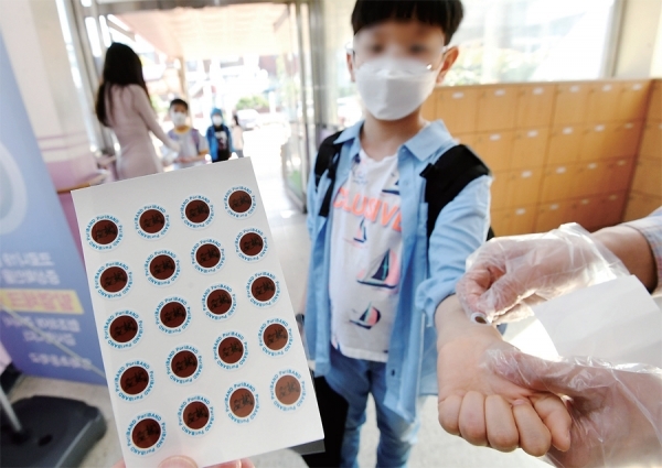 지난 29일 오전 수원 영화초등학교에서 교사들이 등교하는 학생들에게 ‘붙이는 체온계’를 붙여주고 있다. 코로나19 예방을 위해 개발된 ‘붙이는 체온계’는 체온이 37.5도 이상일때 색상이 변하는 스티커로‚ 교사나 학부모가 학생들의 발열상황을 즉시 알 수 있다. 김시범기자