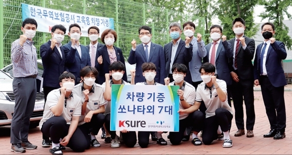 한국무역보험공사가 경기자동차과학고교에 자동차 8대를 기증하고 다 같이 기념사진을 찍고 있다.