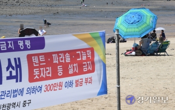 사회적 거리두기 2단계 시행으로 조기 폐장한 인천시 중구 영종도 왕산해수욕장이 첫 주말을 맞은 23일 오후 안내 현수막을 무시한 채 한 나들이객이 파라솔을 설치해 앉아 있다. 장용준기자