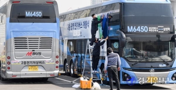 21일 오전 인천 연수구 송도국제도시내 M6450 버스차고지에서 관계자들이 인천 송도국제도시와 서울 강남을 오가는 광역노선에 새롭게 투입할 2층 전기버스에 개통식을 알리는 래핑작업을 하고 있다. 오는 26일부터 본격 운행할 예정인 이 버스에는 70명(1층 11석, 2층 59석)의 승객이 탑승해  환경부 인증 기준으로 1회 충전 시 최대 447km를 주행할 수 있다. 장용준기자