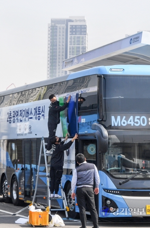 21일 오전 인천 연수구 송도국제도시내 M6450 버스차고지에서 관계자들이 인천 송도국제도시와 서울 강남을 오가는 광역노선에 새롭게 투입할 2층 전기버스에 개통식을 알리는 래핑작업을 하고 있다. 오는 26일부터 본격 운행할 예정인 이 버스에는 70명(1층 11석, 2층 59석)의 승객이 탑승해  환경부 인증 기준으로 1회 충전 시 최대 447km를 주행할 수 있다. 장용준기자
