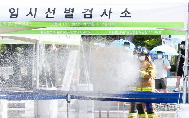 인천지역에 폭염경보가 내려진 26일 오후 남동구 중앙공원 코로나19 임시 선별검사소에서 남동소방서 소방관들이 검사소 주변 열기를 식히기 위해 물을 뿌리고 있다. 인천소방본부는 운영중인 10개의 임시선별검사소에 오전 10시와 오후 2시(폭염경보시 오후 4시)등 1일 2회 물을 뿌릴 계획이다. 장용준기자
