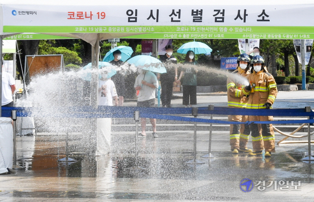 인천지역에 폭염경보가 내려진 26일 오후 남동구 중앙공원 코로나19 임시 선별검사소에서 남동소방서 소방관들이 검사소 주변 열기를 식히기 위해 물을 뿌리고 있다. 인천소방본부는 운영중인 10개의 임시선별검사소에 오전 10시와 오후 2시(폭염경보시 오후 4시)등 1일 2회 물을 뿌릴 계획이다. 장용준기자