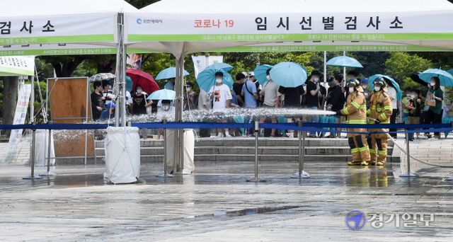 인천지역에 폭염경보가 내려진 26일 오후 남동구 중앙공원 코로나19 임시 선별검사소에서 남동소방서 소방관들이 검사소 주변 열기를 식히기 위해 물을 뿌리고 있다. 인천소방본부는 운영중인 10개의 임시선별검사소에 오전 10시와 오후 2시(폭염경보시 오후 4시)등 1일 2회 물을 뿌릴 계획이다. 장용준기자