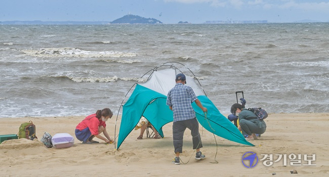 6일 오후 안산시 대부도 방아머리해수욕장을 찾은 시민들이 강한바람에 텐트 보강작업을 하고 있다. 윤원규기자