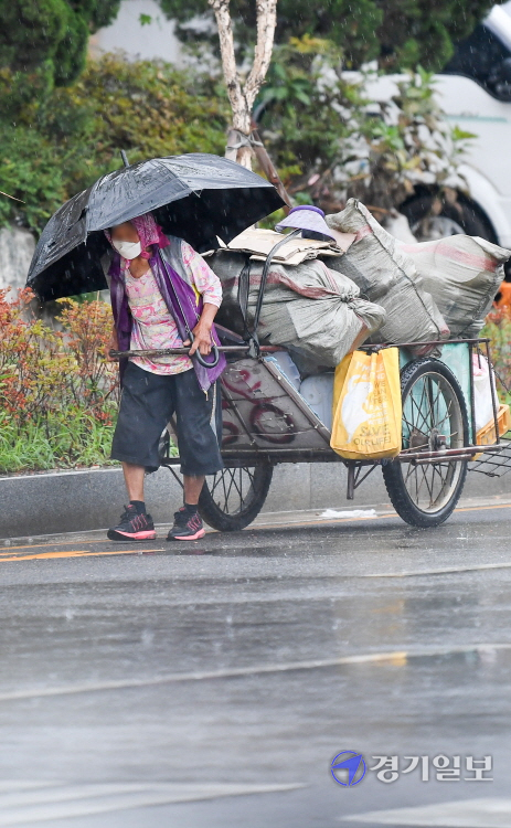 강한 소나기가 내린 18일 오전 인천 부평구 산곡동에서 한 노인이 힘겨운 모습으로 우산과 함께 고물로 가득 채워진 손수레 손잡이를 부여 잡고  인근 고물상으로 향하고 있다. 장용준기자