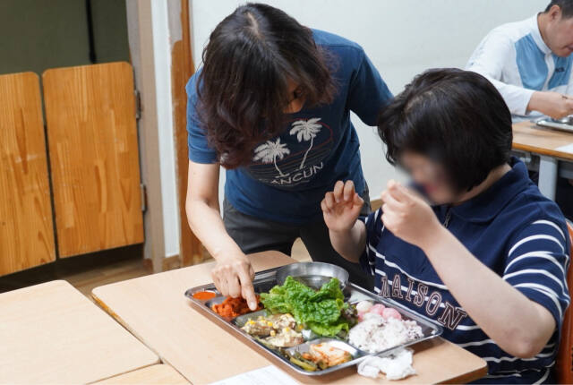 장기근속 유급휴가자 사회복지대체인력으로 ‘늘푸른샘’에서 근무 중인 류미경 사회복지사가 시각장애가 있는 이용인에게 반찬을 설명해주고 있다. 인천 사서원 제공