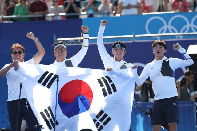 30일(한국시간) 프랑스 파리 레쟁발리드 양궁 경기장에서 열린 2024 파리올림픽 양궁 남자 단체 결승전서 개최지 프랑스를 꺾고 3연패를 달성한 한국 선수단이 태극기를 펼쳐들고 환호하고 있다. 왼쪽부터 박성수 감독, 김우진, 이우석, 김제덕.연합뉴스